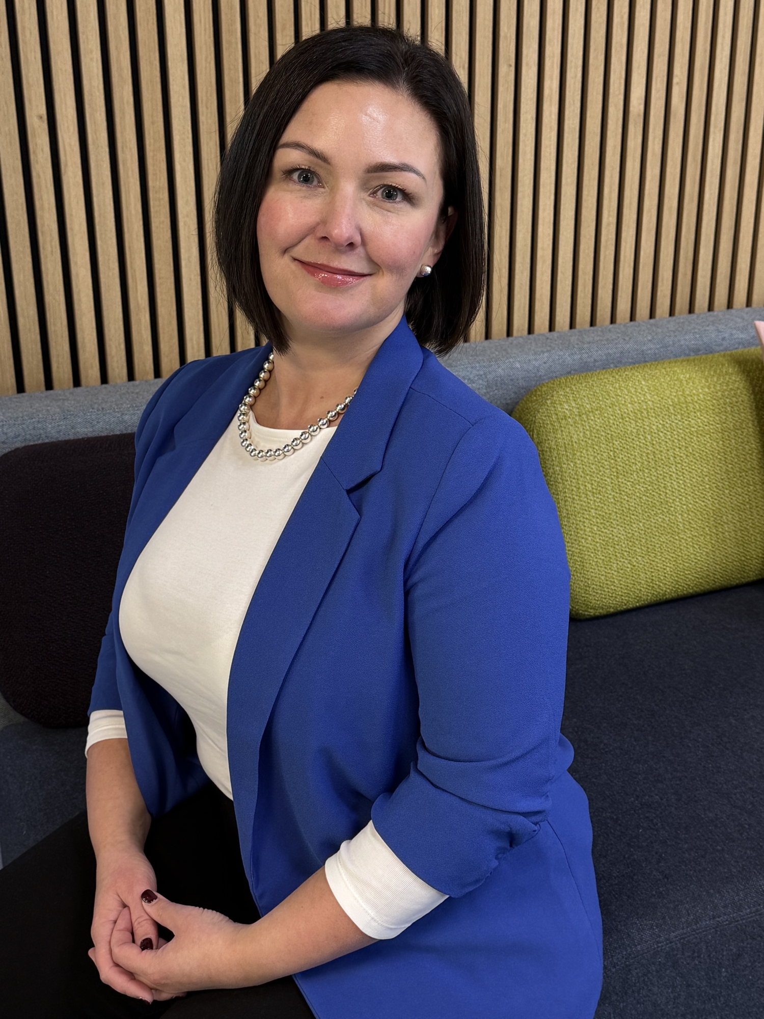 A lady with short, brown hair wearing a blue blazer over a white top.